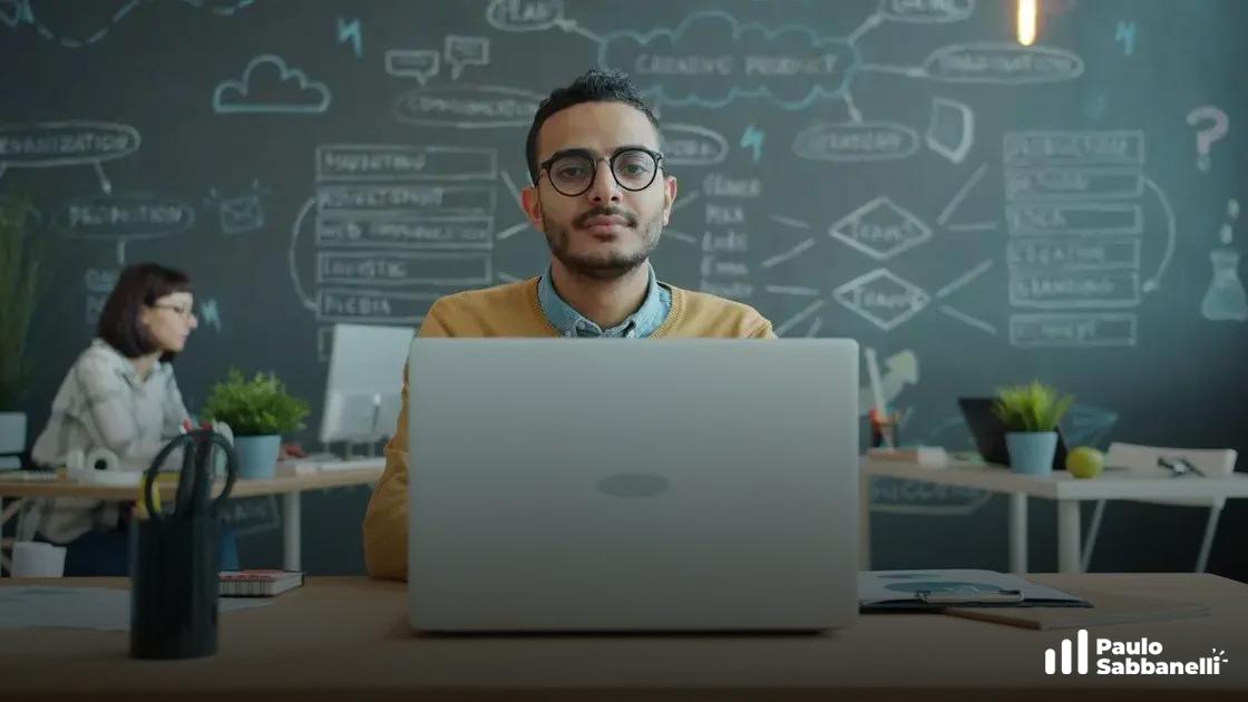 Homem de óculos sentado ao notebook em escritório, com quadro cheio de ideias e diagramas ao fundo