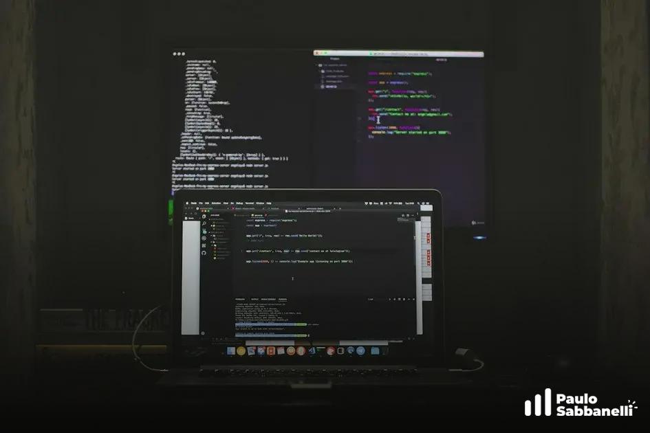 Setup noturno com dois monitores conectados a um notebook, ambos exibindo código na tela