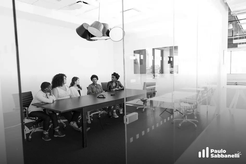 Grupo de mulheres reunidas em sala de vidro com escultura suspensa no teto, foto em preto e branco