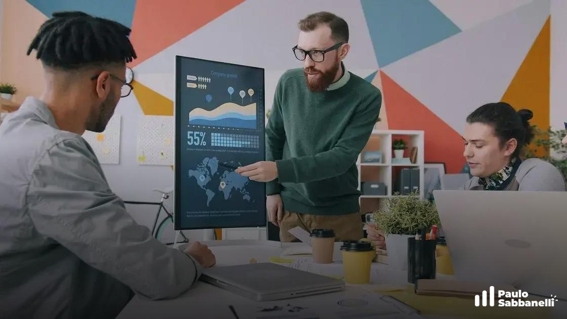 Equipe reunida observa monitor com gráficos e mapa enquanto um homem de suéter verde aponta a tela