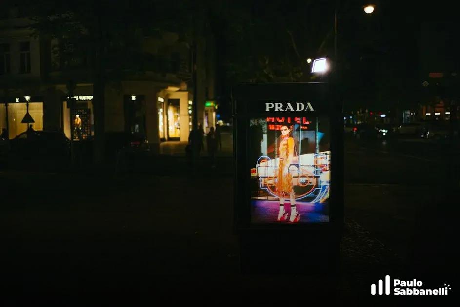 Painel publicitário iluminado da marca Prada em ponto de ônibus durante a noite