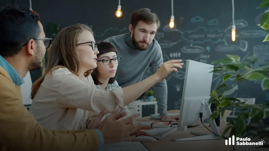 Quatro colegas observam monitor enquanto homem aponta para a tela em escritório