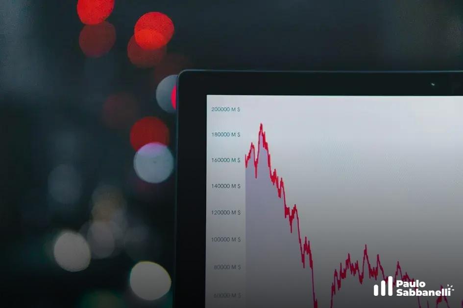 Tela de notebook mostra gráfico de linha vermelha em queda, com luzes desfocadas ao fundo