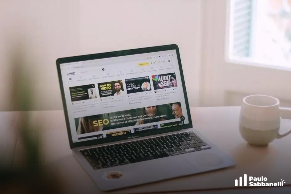 Notebook aberto mostra página de blog sobre SEO com destaque para auditoria, café próximo à janela