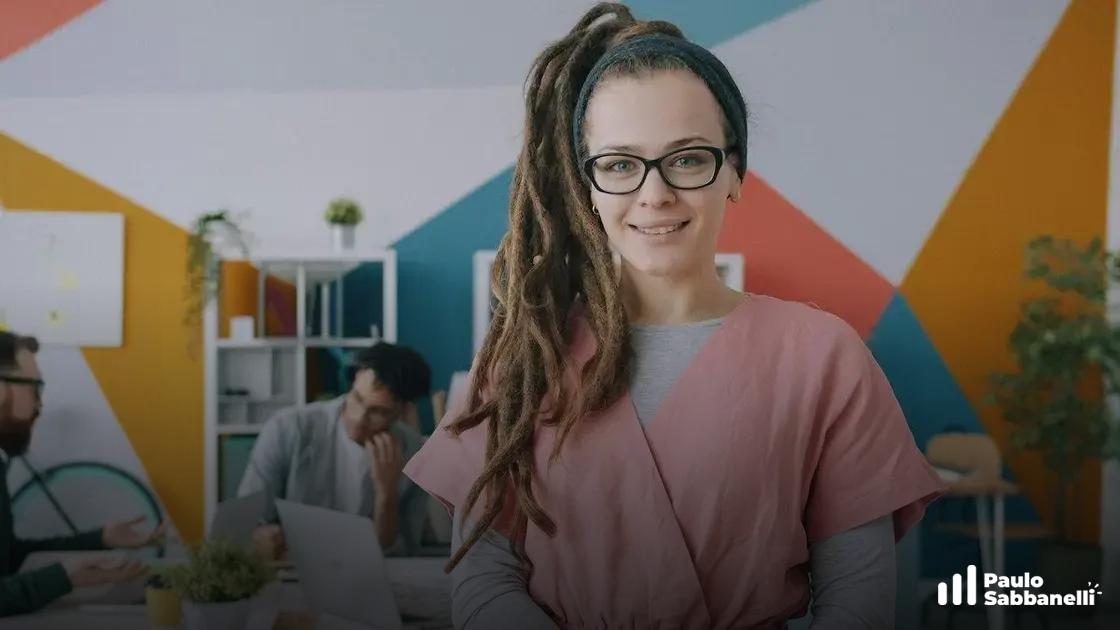 Mulher de dreadlocks sorri em escritório com parede geométrica colorida ao fundo