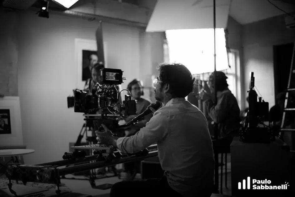 Equipe de filmagem opera câmera em estúdio com iluminação intensa, foto em preto e branco