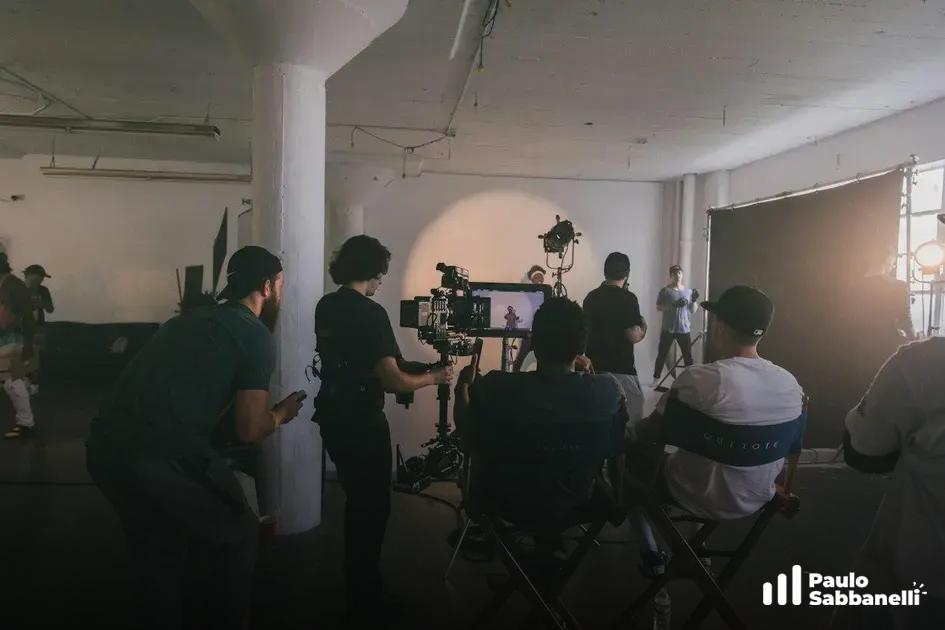 Equipe de filmagem em estúdio industrial ao redor de câmera em tripé com luz de apoio
