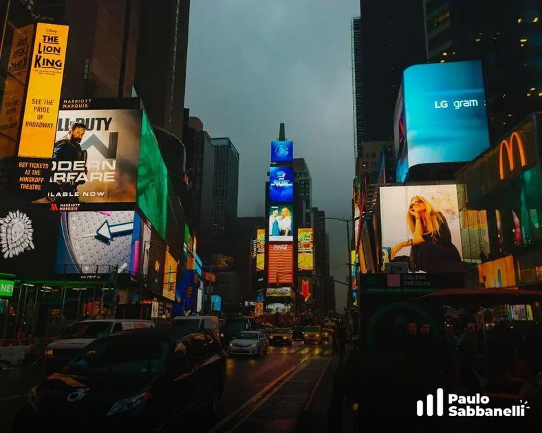 Times Square ao anoitecer com diversos painéis publicitários iluminados e trânsito intenso