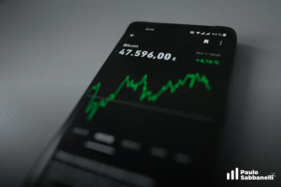 Celular exibe gráfico de preço do Bitcoin em linha verde sobre fundo escuro