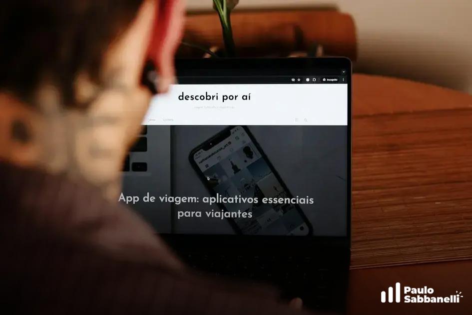 Pessoa observa notebook exibindo app de recomendações com artigo sobre aplicativos de viagem
