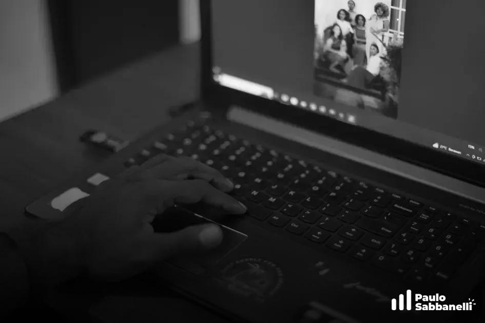 Foto em preto e branco de uma mão no touchpad de um notebook durante videochamada em grupo