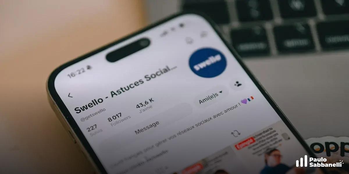 Smartphone sobre teclado de notebook exibindo perfil social da ferramenta Swello