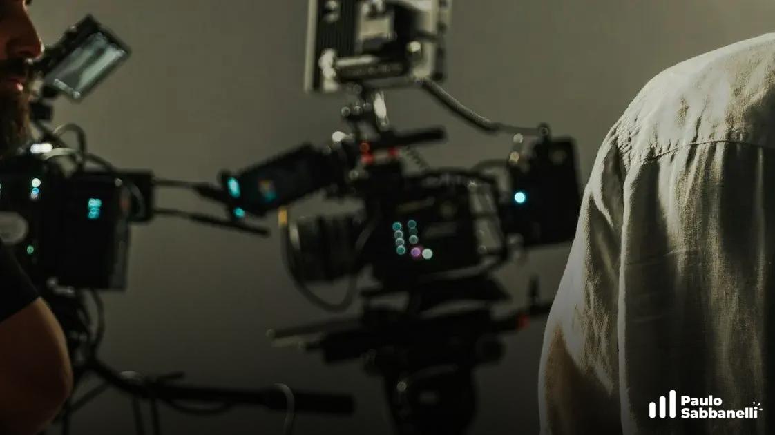 Equipamento de filmagem com monitor e refletores desfocados ao lado de pessoa de camisa clara