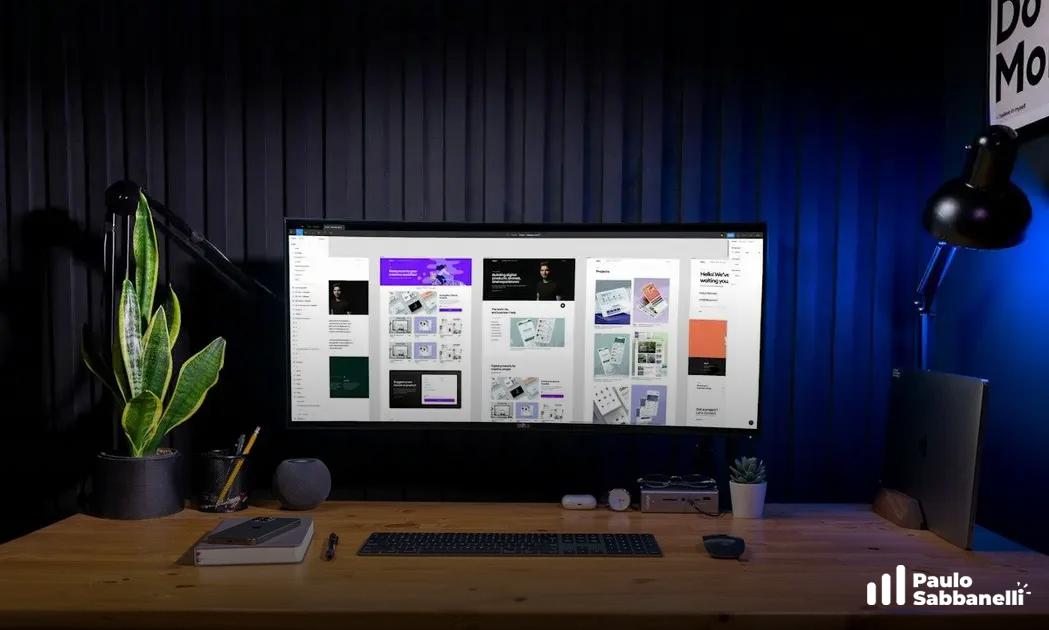 Monitor ultrawide exibe múltiplas janelas de design sobre mesa de madeira em ambiente azulado